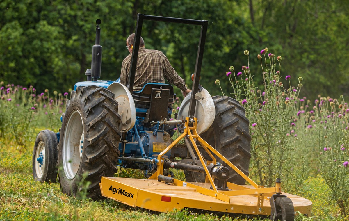 AgriMaxx RC72 rotary cutter mounted on a tractor, cutting a path through a wildflower meadow